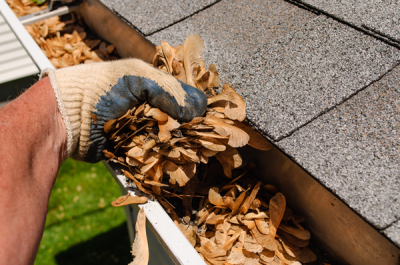 gutter-1 Gloved hand removing dry leaves from a clogged gutter, illustrating gutter cleaning Kirkland to ensure proper water drainage and protect roof integrity.